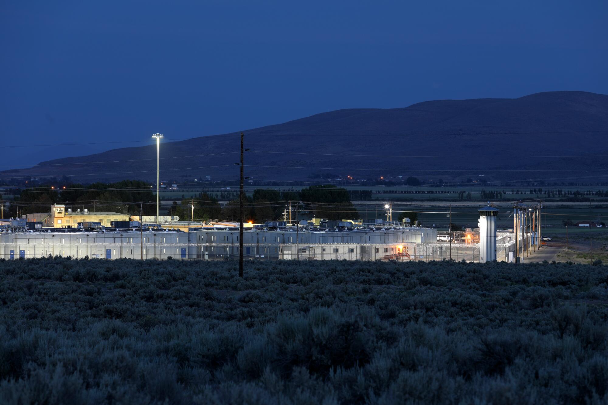 A view from a distance of a fence-enclosed prison at dusk.