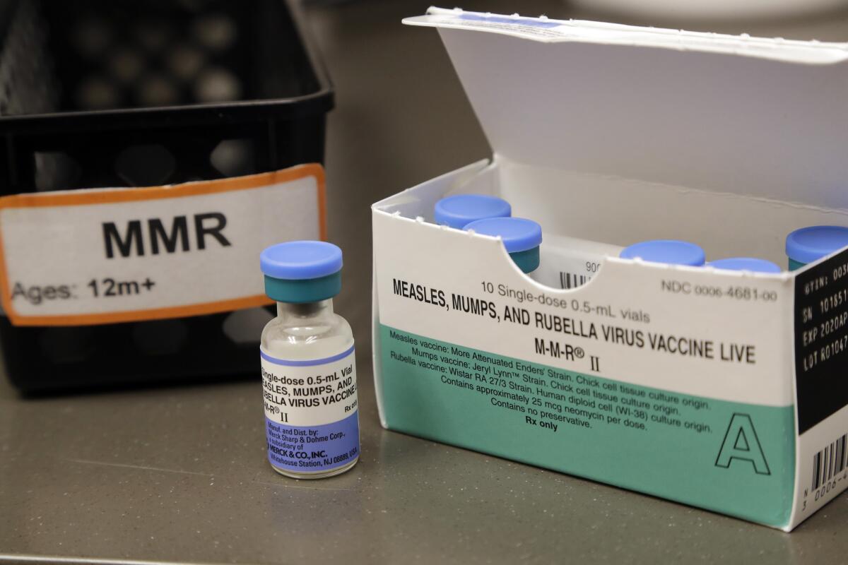 A vial holding a dose of MMR vaccine sits in front of a box of the vials.