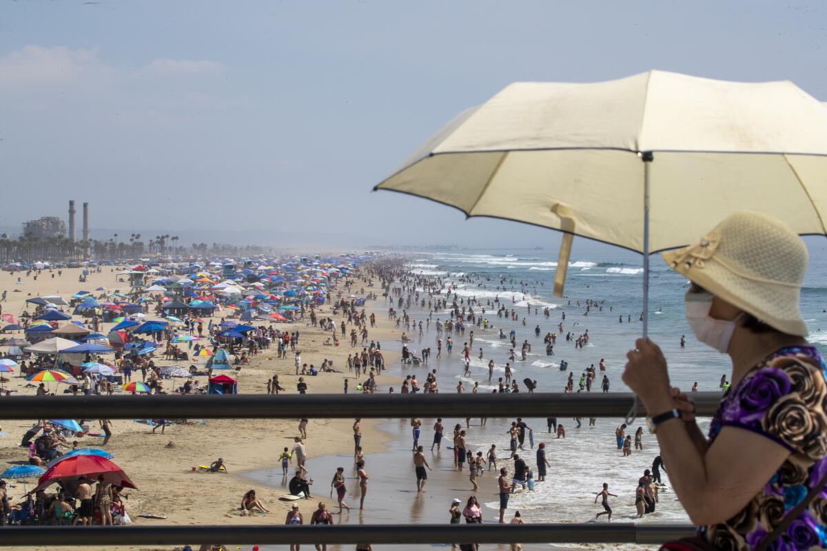 A woman holds an umbrella with a crowded beach in the background