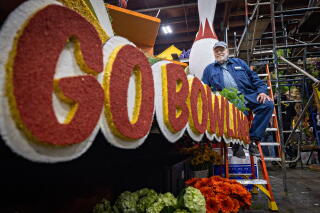 A man sits near a float that says "Go Bowling" in red and yellow, with bouquets of flower underneath