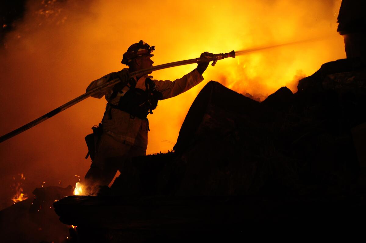 A nighttime photo of a firefighter silhouetted against flames.