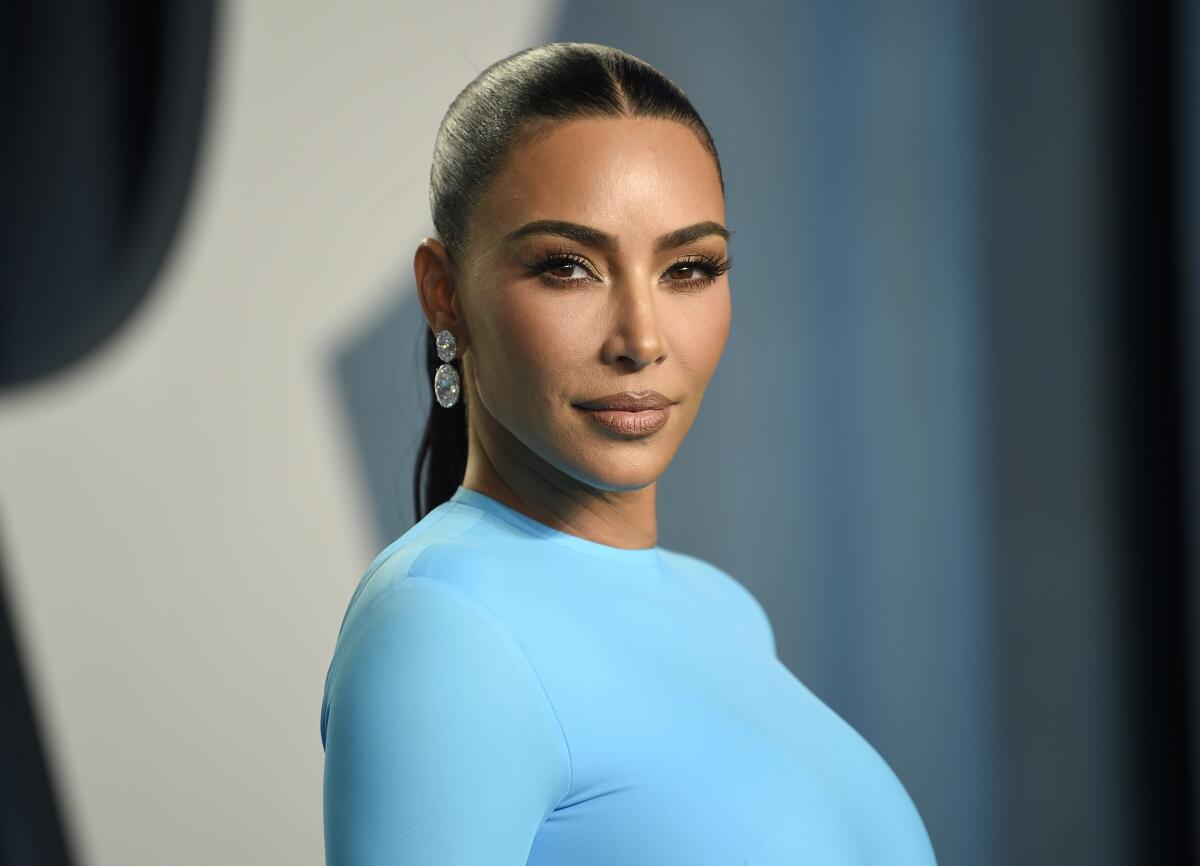 Kim Kardashian with slicked-back hair poses for the camera in a light blue dress.