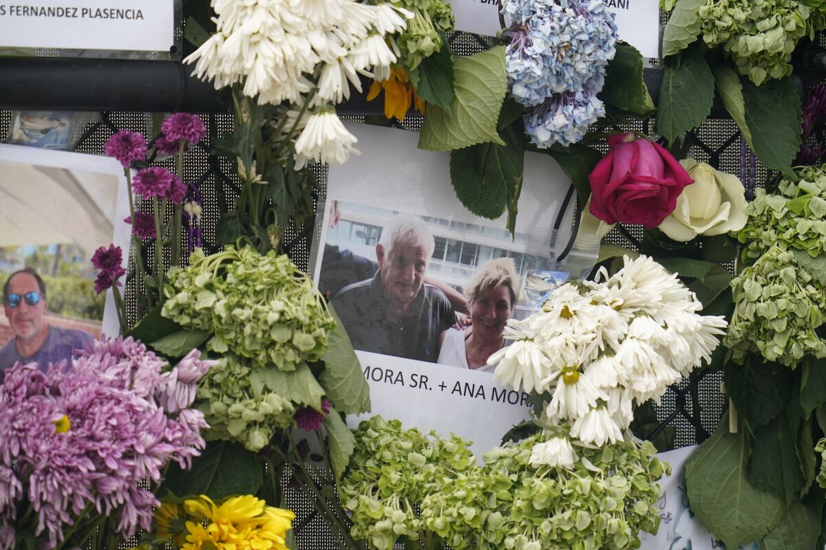 This June 29, 2021, photo shows a memorial wall for the victims of the Champlain Towers South building collapse in Surfside, Fla., with a photo of Juan Mora Sr. and his wife, Ana Mora. (AP Photo/Gerald Herbert)