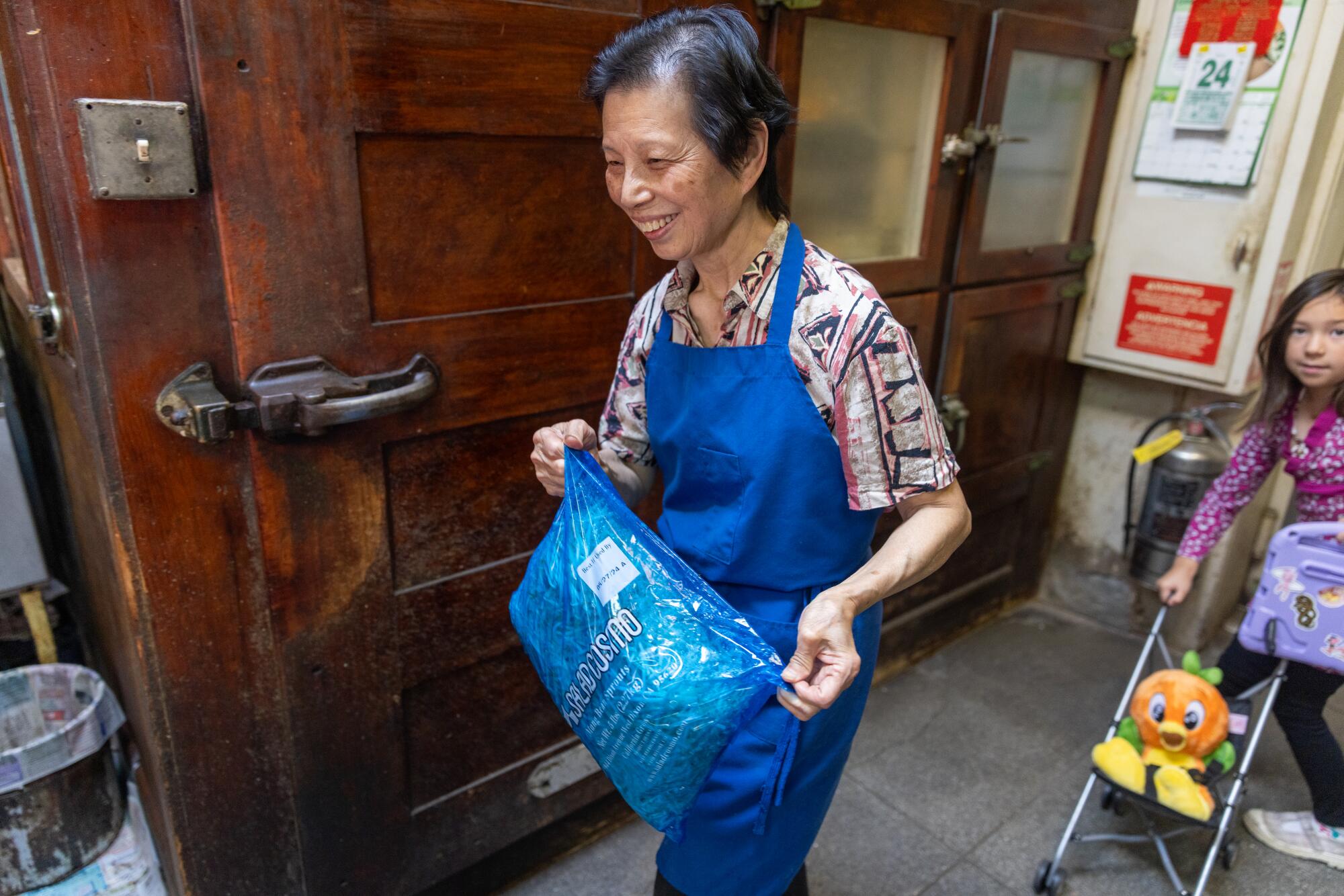 A smiling woman in blue apron gathers ingredients for lunch service.