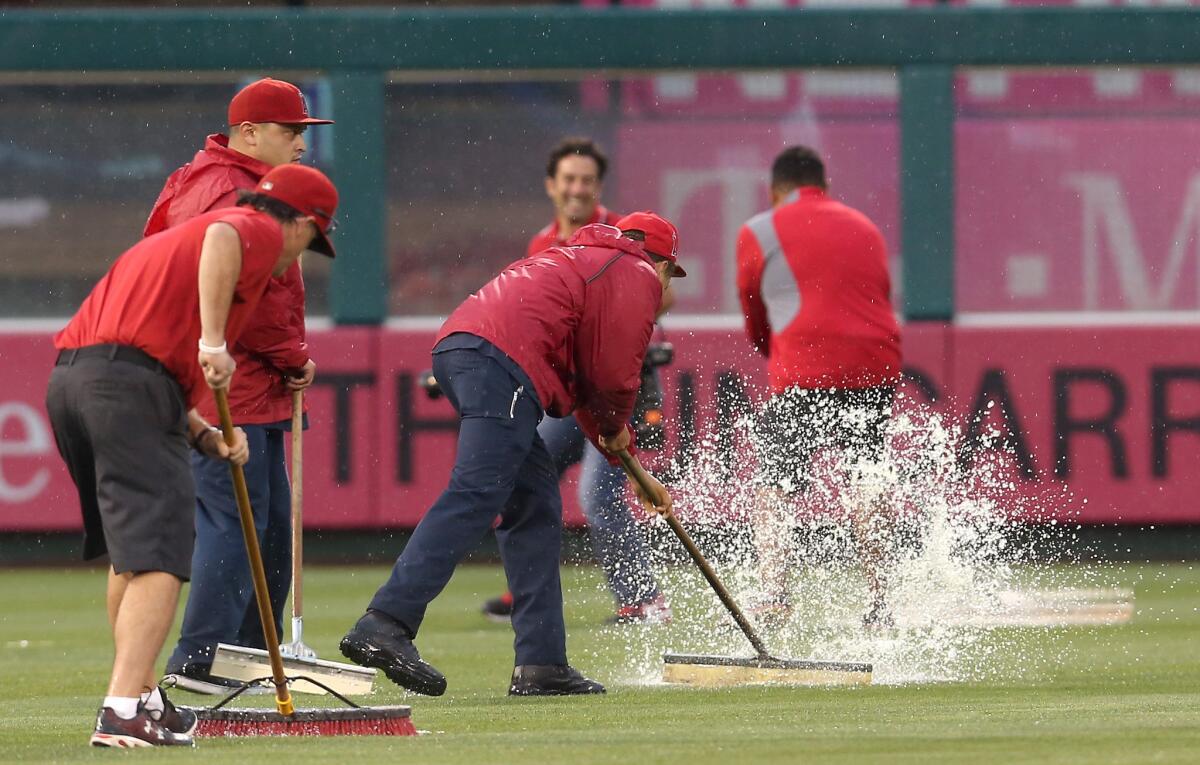 Members of the grounds crew sweep water in the outfield at Angel Stadium before Sunday's game against the Red Sox.