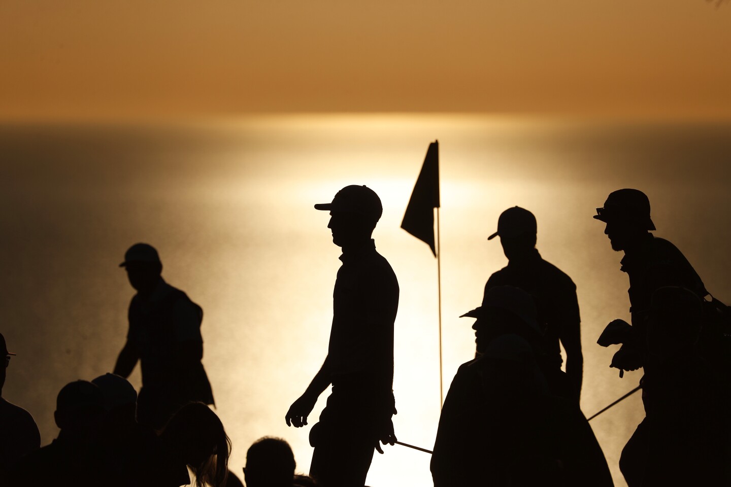 As the sun begins to set, golfers pass the 17th hole during the fourth round of the Farmers Insurance Open.