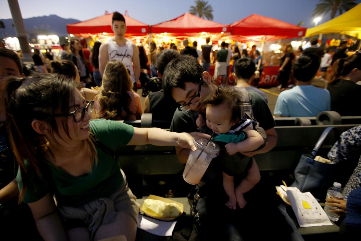 Linda Lee and Sam Man share a cold drink with their daughter, Olivia Man, 6 months, at a crowded 626 Night Market in Arcadia. (Francine Orr / Los Angeles Times)