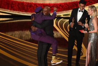 Spike Lee in a purple suit and golden Air Jordans is jumping into the arms of Samuel L. Jackson on the Oscars stage