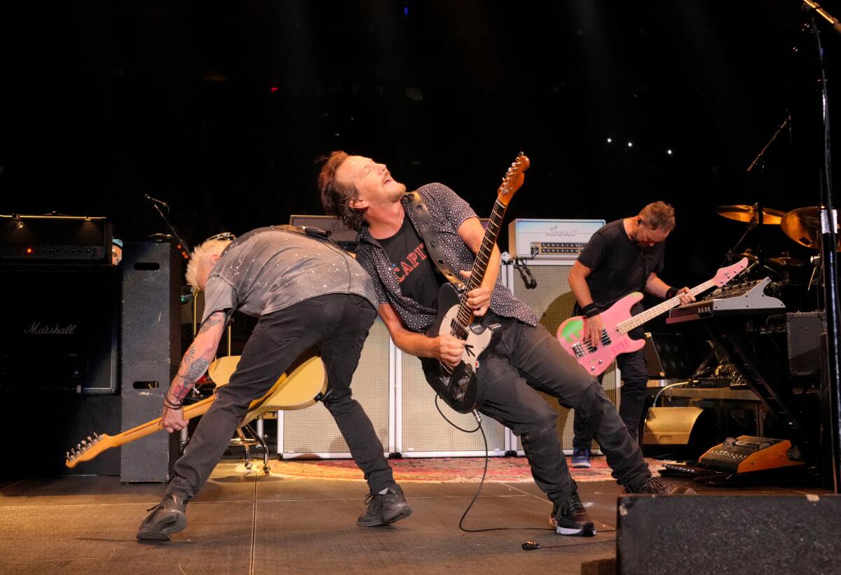 Mike McCready and Eddie Vedder and members of Pearl Jam are leaning against each other while strumming guitars on stage