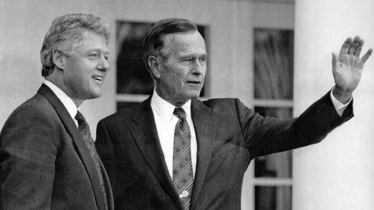 President George H.W. Bush waves as President-elect Bill Clinton stands alongside at the White House on Nov. 18, 1992