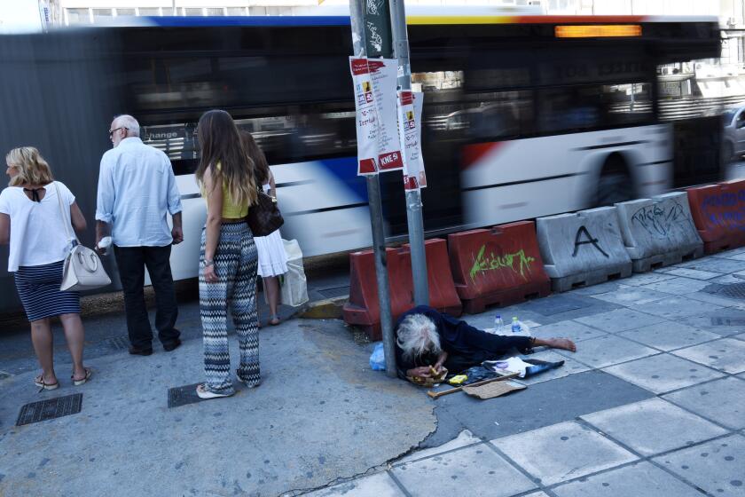 People wait to cross a street as an elderly woman begs for money in the northern Greek city of Thessaloniki on Aug. 18, 2015.