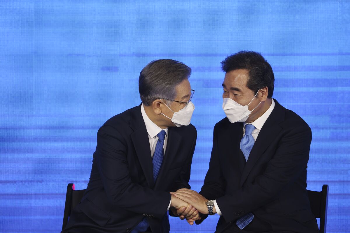 Lee Jae-myung shakes hands with Lee Nak-yon in front of a blue background