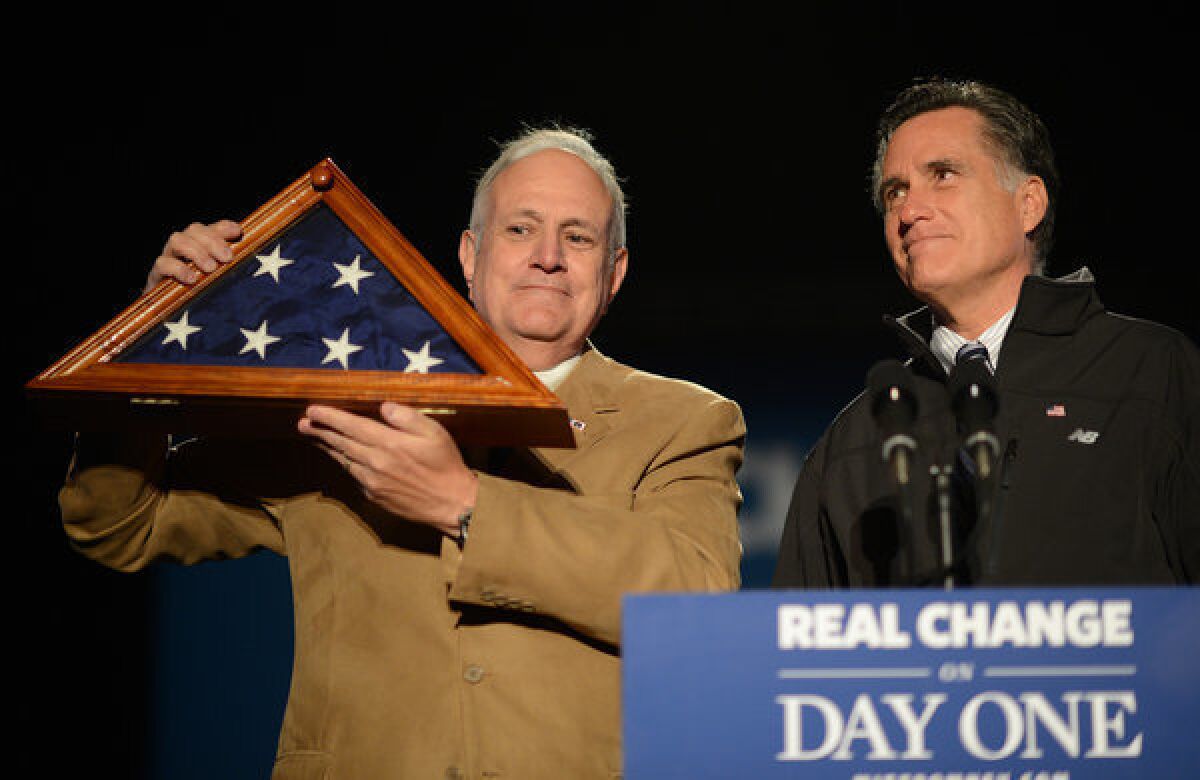 At a campaign event in Colorado, Mitt Romney looks on as scoutmaster Bill Tolbert displays a U.S. flag recovered from the wreckage of the space shuttle Challenger. Romney often shares an inspiring story about the flag.