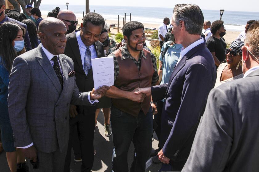 Manhattan Beach, CA - September 30: California Senator Steven Bradford, left holds a signed SB 796, with former Manhattan Beach, CA., Mayor Mitch Ward, as Anthony Bruce, great-great grandson of Charles and Willa Bruce shakes hands with Gov. Gavin Newsom, after Newsom's signing of SB 796, authored by Bradford, which authorized the return of ocean-front land to the Bruce family, during a press conference held at Bruce's Beach in Manhattan Beach, CA, Thursday, Sept. 30, 2021. Some of the land making up Bruce's Beach was purchased by African American couple Willa and Charles Bruce, in 1912, establishing a resort that was open to African Americans. But by the 1920s, racial tensions grew in the beach community and the city condemned the properties. The park was renamed multiple times over the next 80 years and in 2007, was re-named for the Bruce family, responsible for trying to bring change and equality to the city. (Jay L. Clendenin / Los Angeles Times)