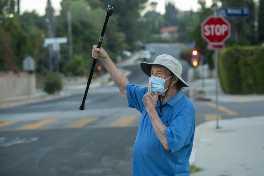 PORTER RANCH, CA - OCTOBER 19, 2020: Charles Dirks, 81, gestures for a motorist to wear a facial covering to protect against the spread of the coronavirus, as he walks along Vanalden Ave. Porter Ranch. Dirks, a retired political science professor, tries to get the attention of every person he sees during his twice daily walks near his home in Porter Ranch, congratulating those that wear protective facial covering and berating those that don't. (Mel Melcon / Los Angeles Times)