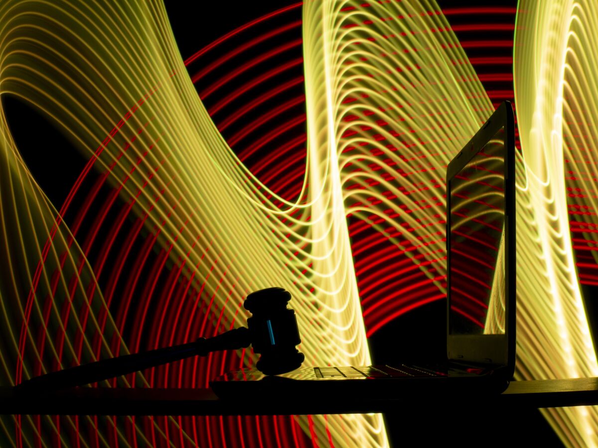 Judge's gavel on an open laptop, against a background of yellow and red swirl of lines
