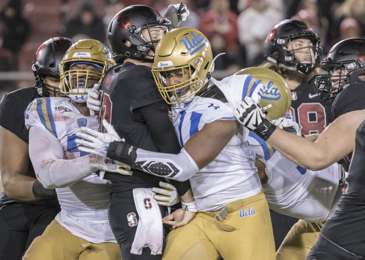 UCLA's Osa Odighizuwa (left) and Keisean Lucier-South hit Stanford quarterback Jack West.