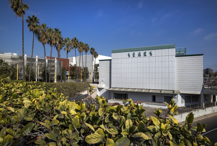 Exterior of a vacant Streamline Moderne style Sears store with a row of palm trees nearby