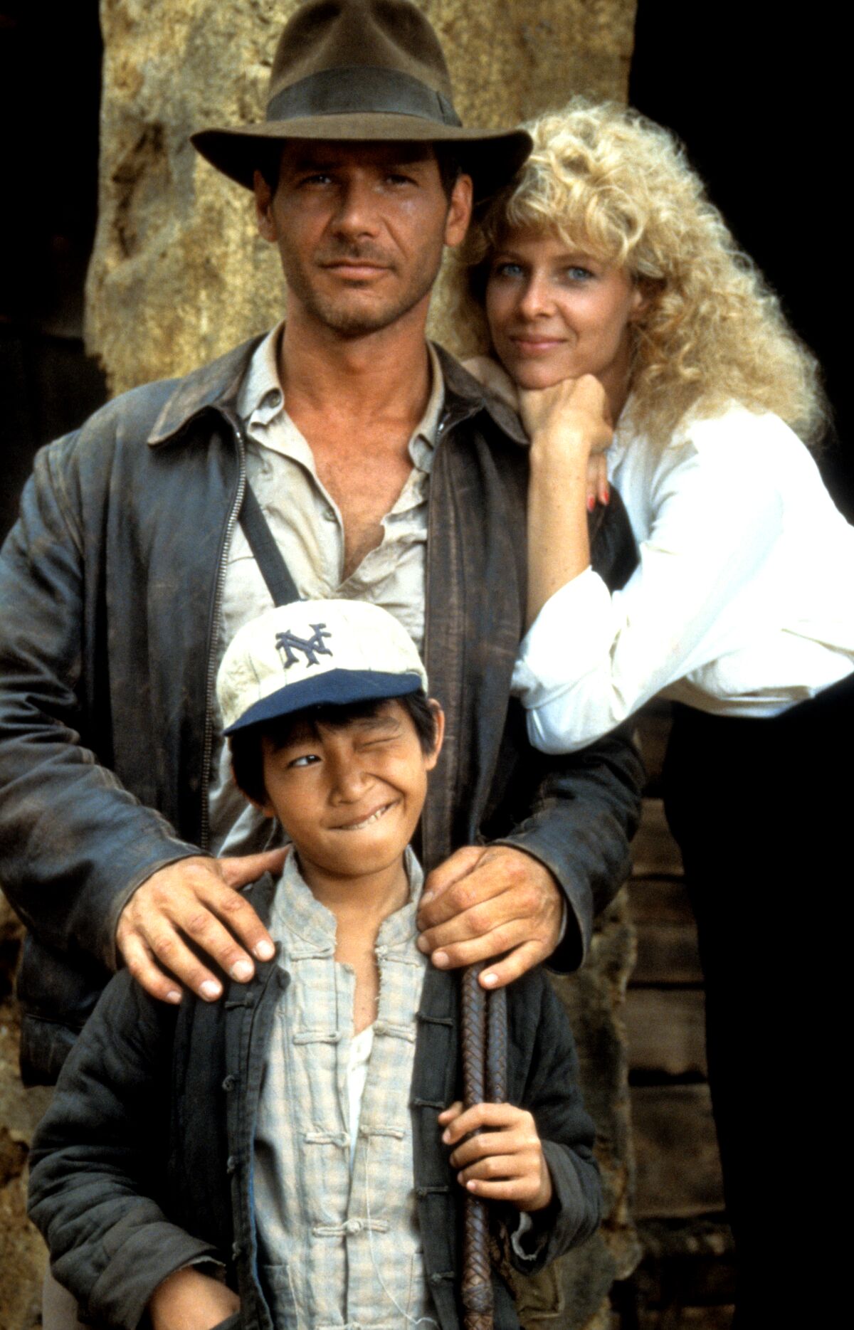 A man in a brown hat and a woman with curly blond hair posing with a child in a baseball cap