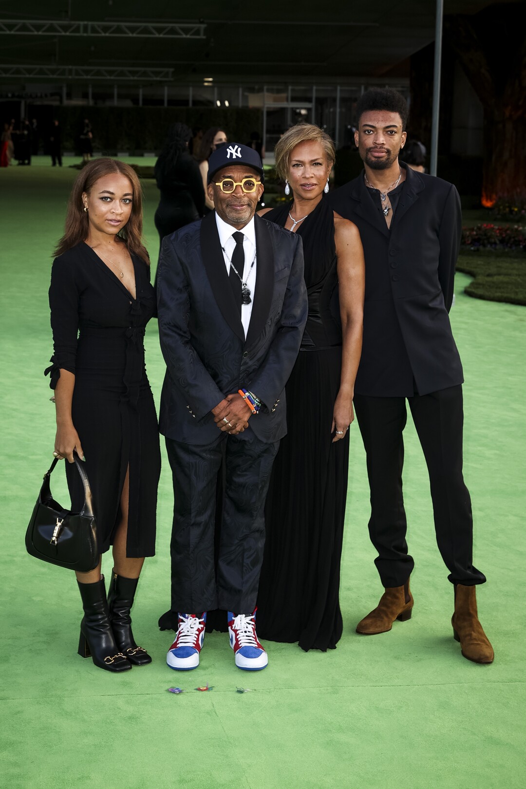 A family of four posing in black, formal attire on a green carpet