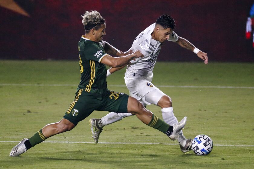 FILE - Portland Timbers defender Pablo Bonilla, left, and LA Galaxy forward Cristian Pavon vie for the ball during the second half of an MLS soccer match in Carson, Calif., in this Wednesday, Oct. 7, 2020, file photo. Major League Soccer has extended its deadline for negotiating adjustments to the existing collective bargaining agreement until Feb. 4 and warned it is prepared to lock out players if a deal isn't reached by then. (AP Photo/Ringo H.W. Chiu, File)
