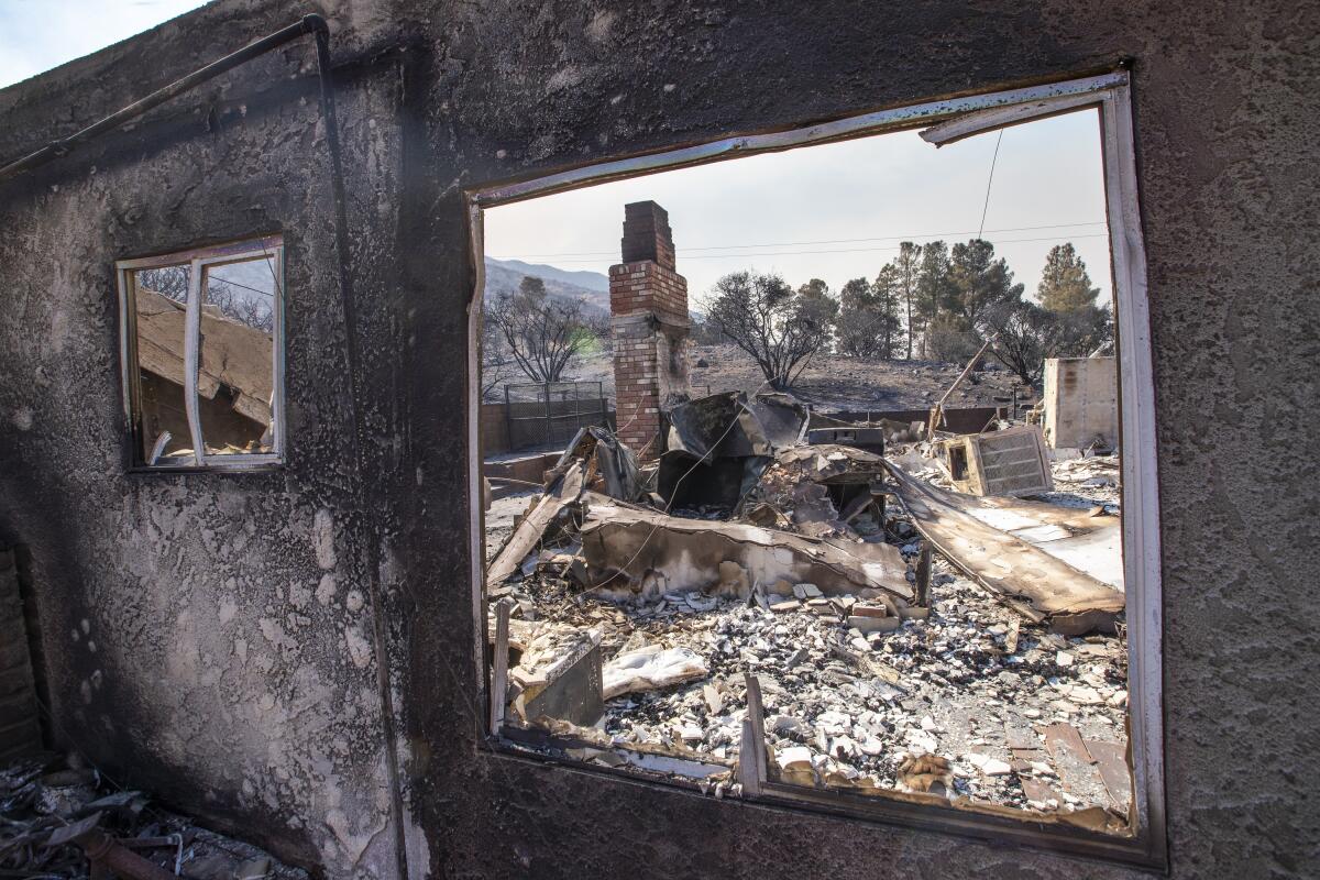 A blackened wall stands, with rubble of a home seen through the empty window frame