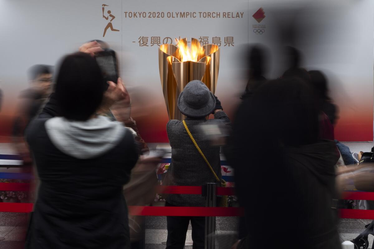 People take photos with their mobile phones of an Olympic flame display.