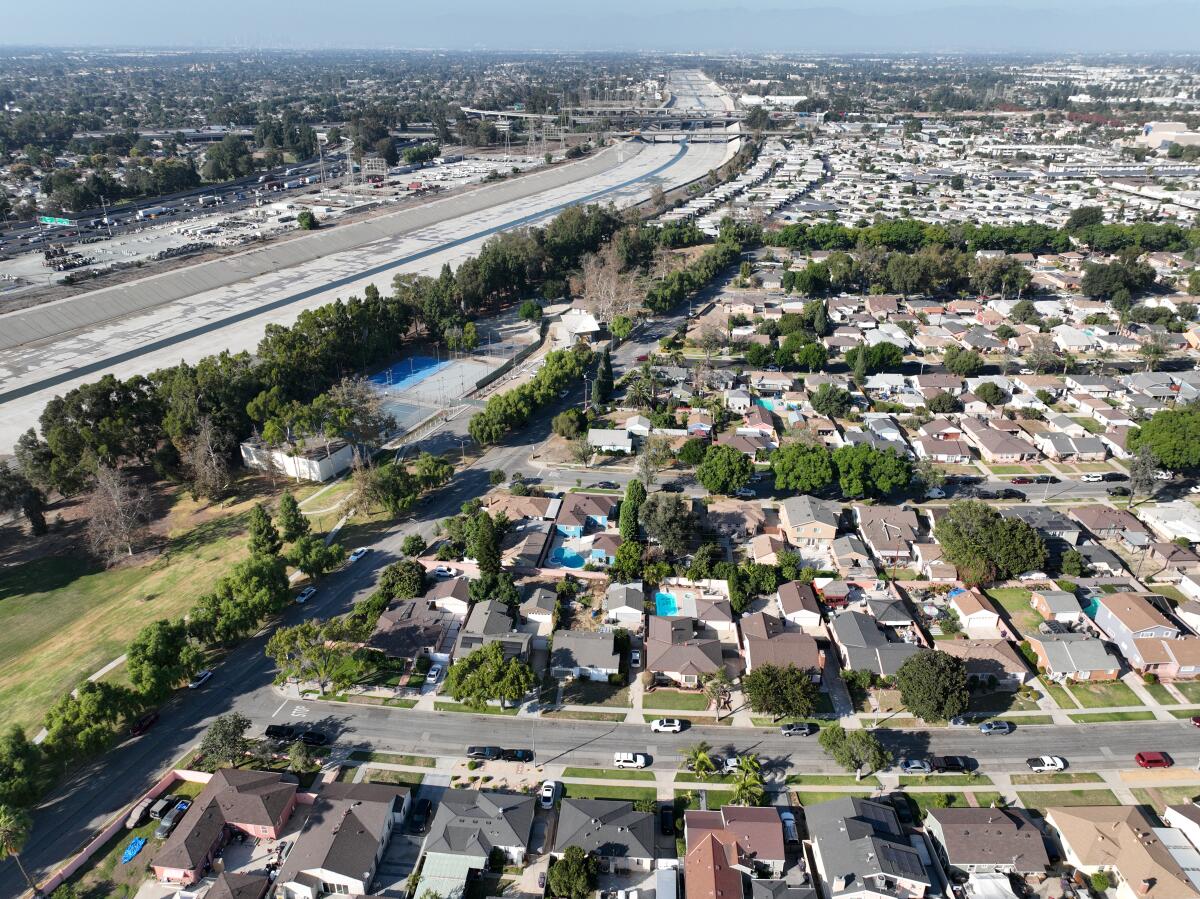 An aerial view of a concrete river channel bordered by blocks of homes.