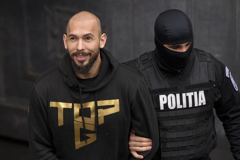 A police officer escorts Andrew Tate, handcuffed, from the Court of Appeal in Bucharest, Romania