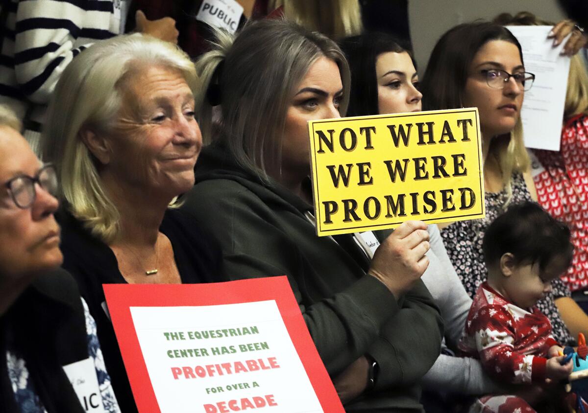 People hold signs in support of the equestrian center during the OC Fair & Event Center board meeting on Dec.14, 2023. 