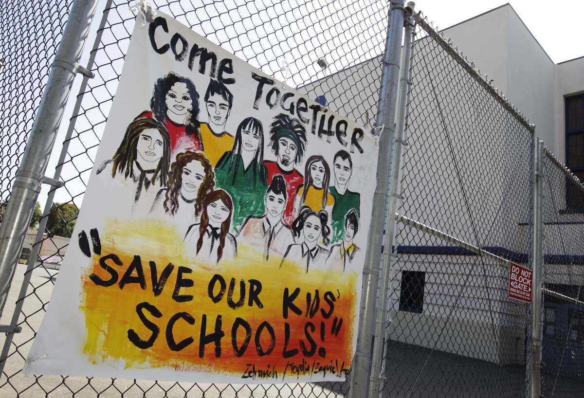 A sign hanging on a fence reads "come together, save our kids' schools"