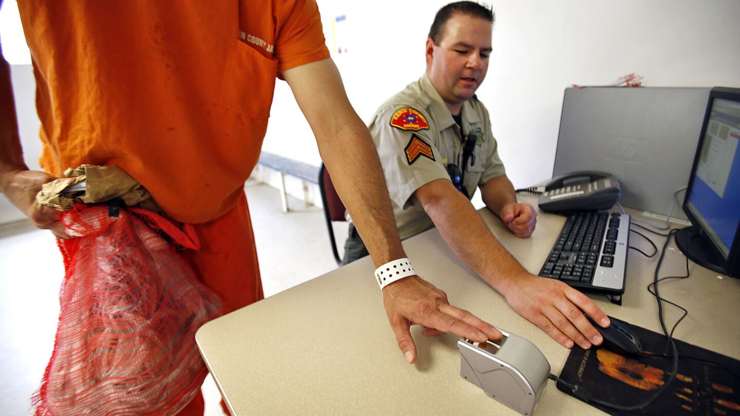 Kern County Sheriff Sgt. Mike Dobbs, right, processes an inmate using fingerprint technology to identify subjects for early release.