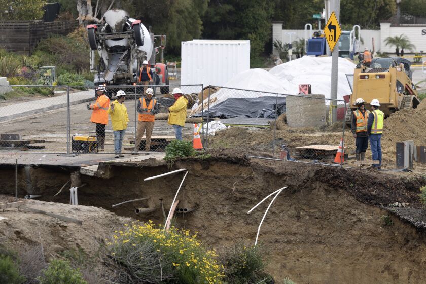ENCINITAS, CA - MARCH 11, 2023: Workers stand near a large sinkhole that formed from recent rains at the south end of Lake Drive in Cardiff on Saturday, March 11, 2023. (Hayne Palmour IV / For The San Diego Union-Tribune)