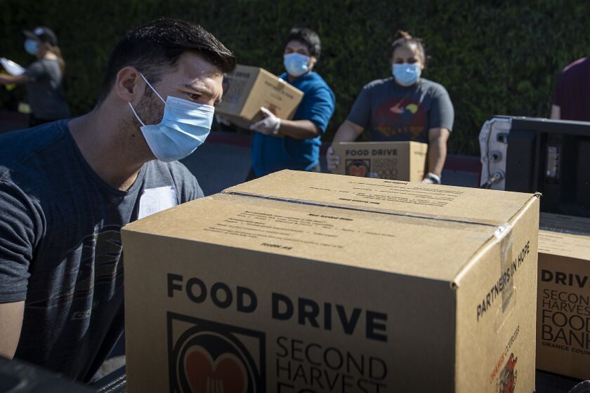 IRVINE, CA -- WEDNESDAY, APRIL 1, 2020: From left: Paul Ewing, Jose Secundino, and Shavonne Budnik, who are all recently hired Second Harvest Food Bank of Orange County temporary employees, and have been laid off from restaurant jobs due to the coronavirus pandemic, load boxes of food into volunteers' trucks that will be delivered to local senior centers in Orange County. Photo taken at Second Harvest Food Bank at the Orange County Great Park in Irvine, CA, on April 1, 2020. (Allen J. Schaben / Los Angeles Times)