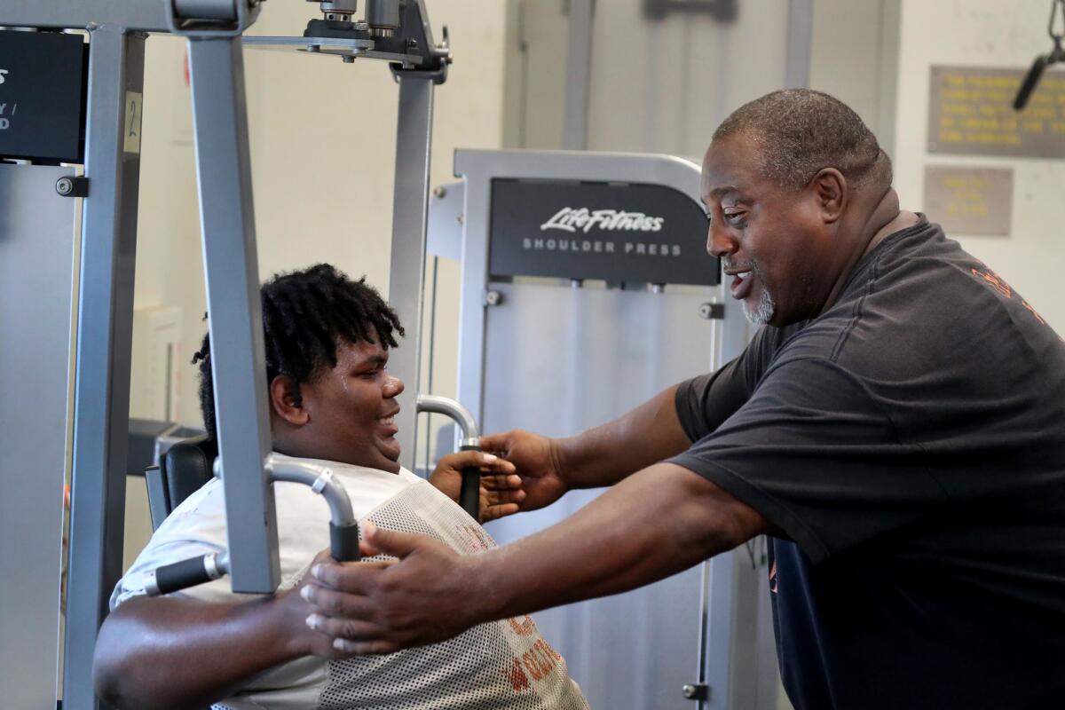 Angelou High football coach Derek Benton works with Steafon Horne, 16, a junior offensive guard, during a weight training session on Tuesday.