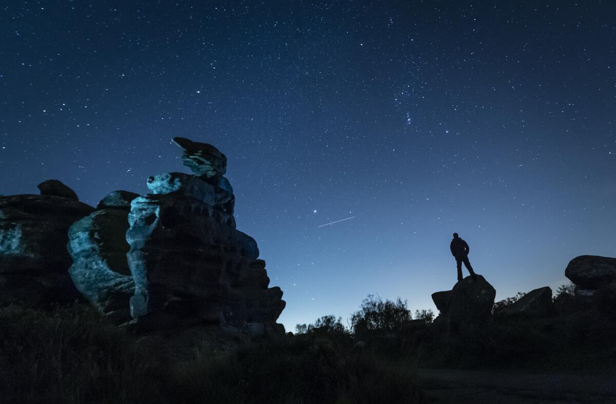 A plane passes by as a man stargazes at Brimham Rocks in Yorkshire as the Orionid meteor shower reaches its peak. 