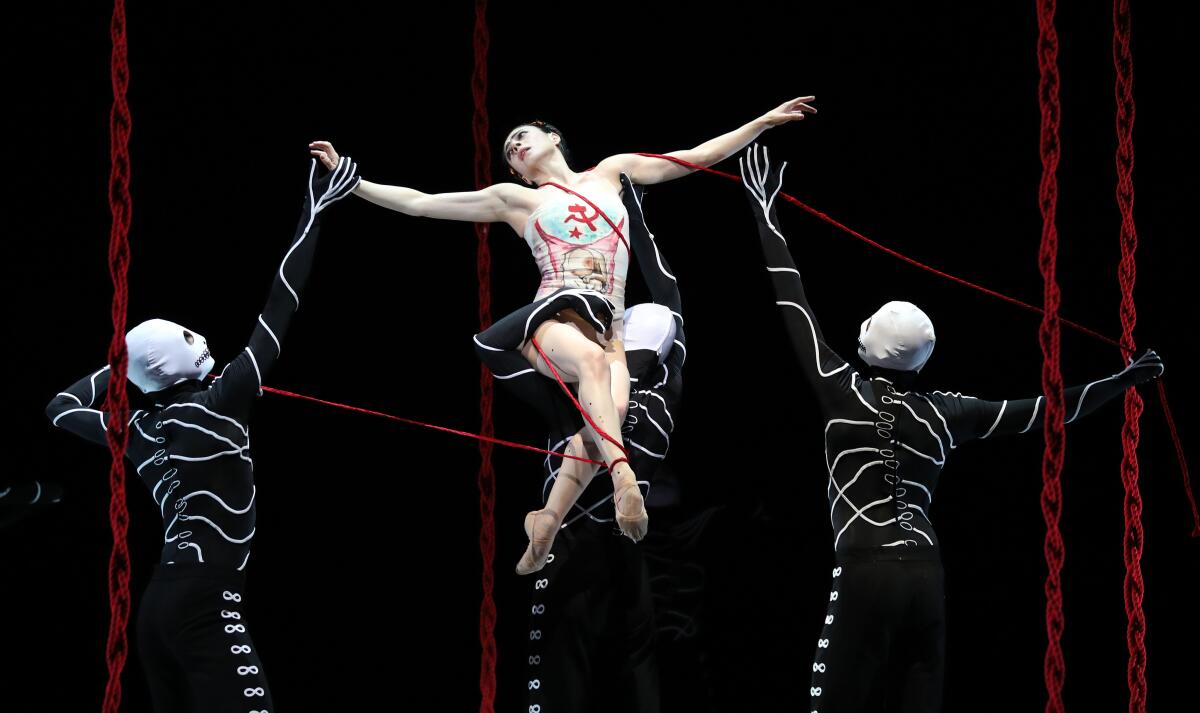 A dancer playing Frida Kahlo wearing a corset is hoisted into the air by three figures dressed as skeletons.