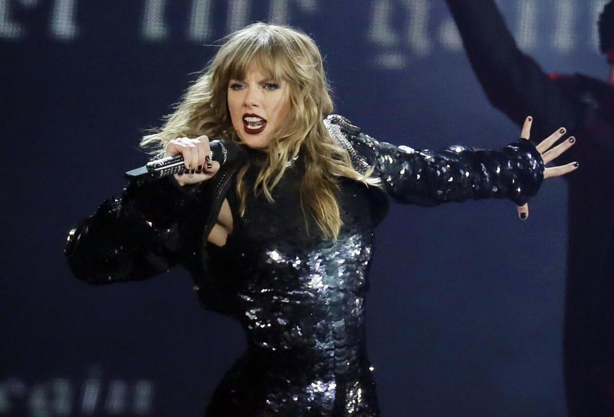 A woman in a shiny black outfit sings into a microphone onstage.