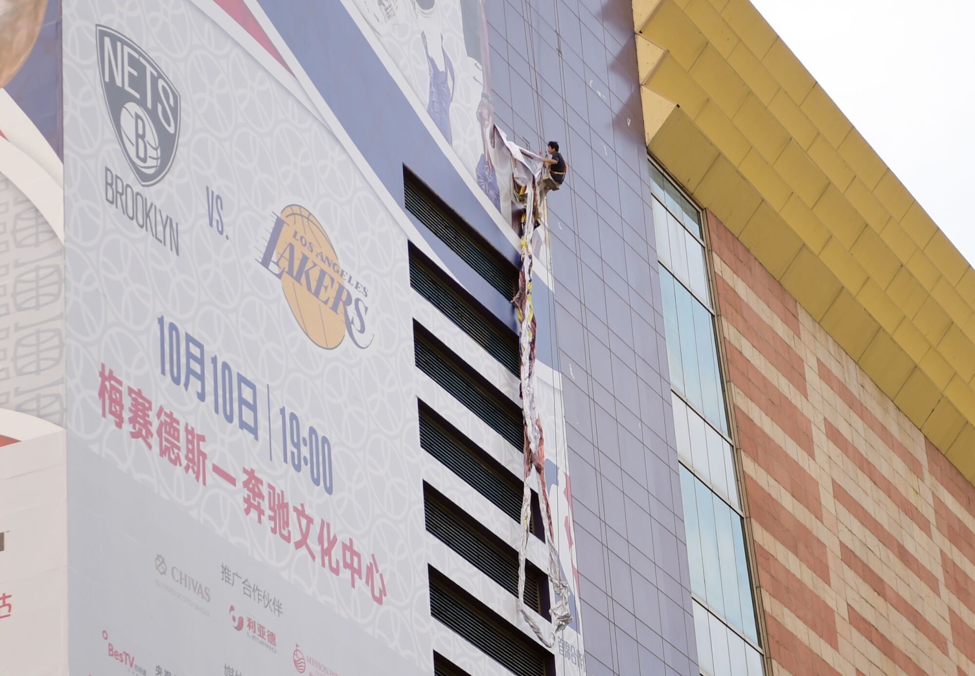 Un trabajador retira un cartel grande que promociona el juego Lakers-Nets en el Lujiazui Zhengda Plaza en Shanghái.