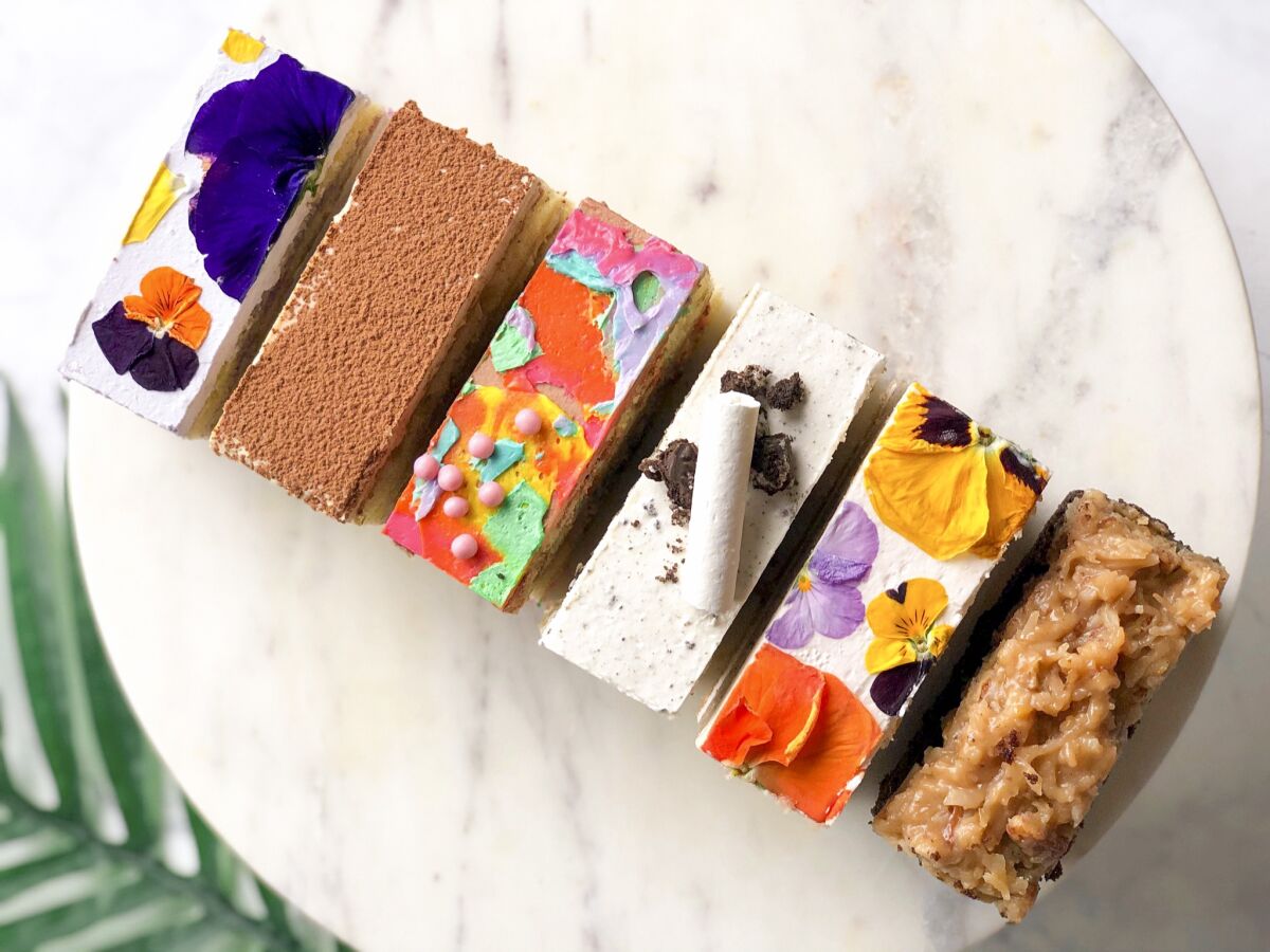 A top-down photo of a diagonal row of colorful, icing-painted rectangular cake bars from bakery Flouring LA.