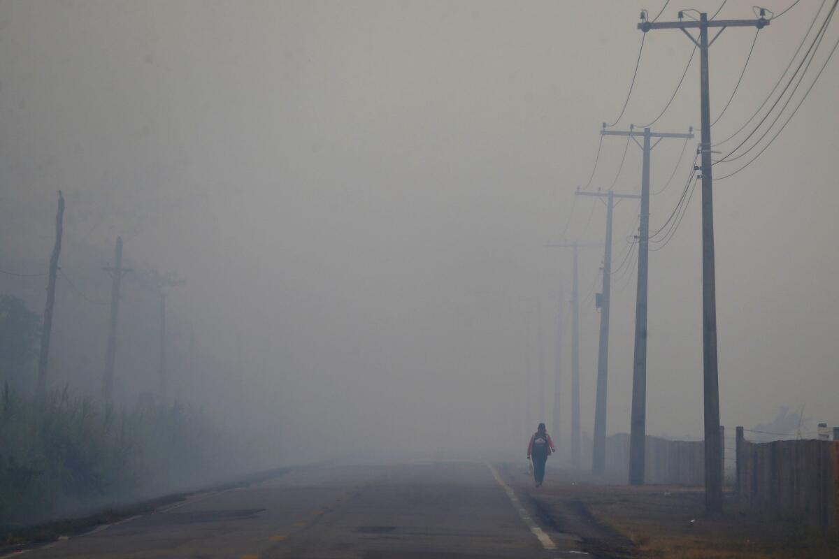 A person walks on the side of a roadway through thick smoke. 