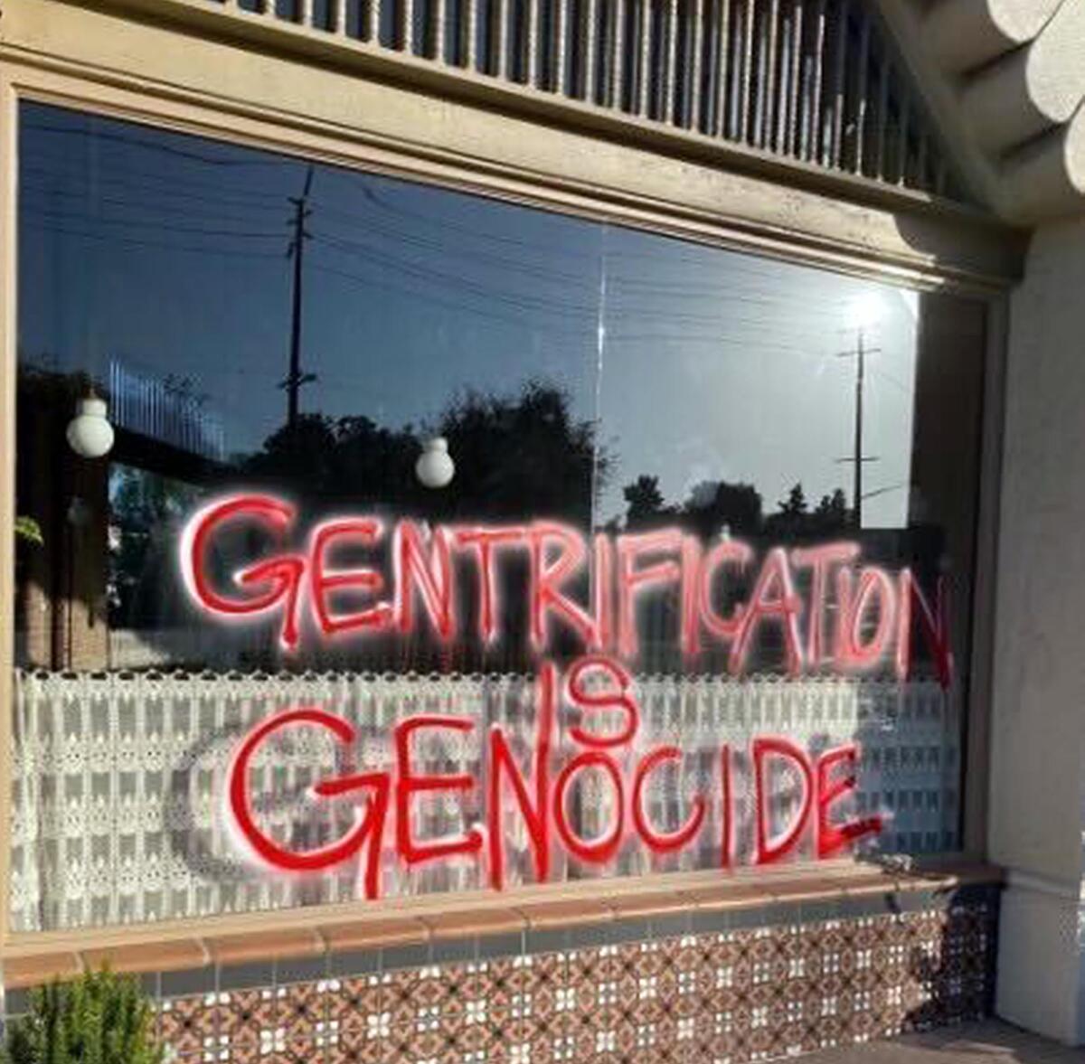 A window spray-painted with the words "Gentrification Is Genocide." 