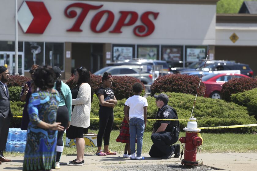 A Buffalo police officer talks to children at the scene of Saturday's shooting at a supermarket on Sunday, May 15, 2022, in Buffalo, N.Y. A white 18-year-old wearing military gear and livestreaming with a helmet camera opened fire with a rifle at a supermarket, killing and wounding people in what authorities described as “racially motivated violent extremism.” (AP Photo/Joshua Bessex)
