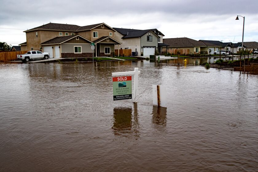 A flooded residential neighborhood. A "Sold" sign is protruding from the muddy water in center.