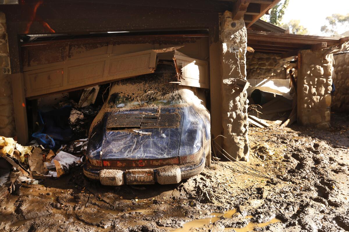 A car is stuck under a broken garage door and surrounded by mud.