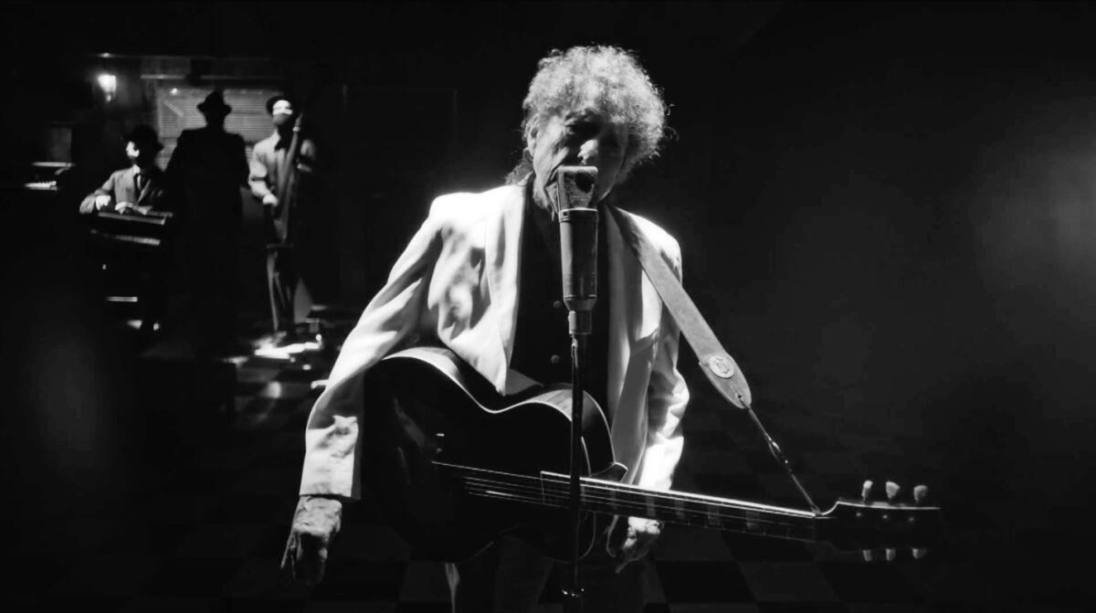 A black and white image of Bob Dylan at a microphone holding a guitar