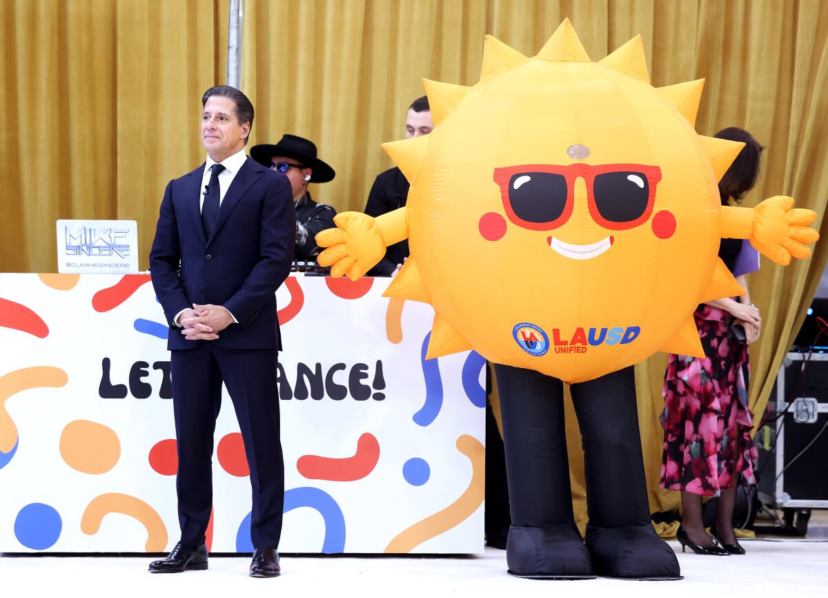 A man stands next to a person dressed in a sun costume.