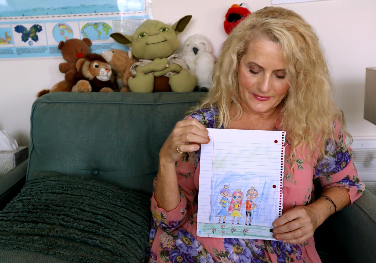 A woman holds a child's drawing on lined paper of a family