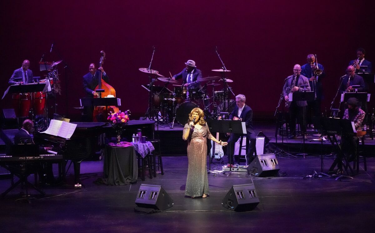 Jennifer Holliday, decked out in a sparkling dress, sings on a stage that also features an orchestra.