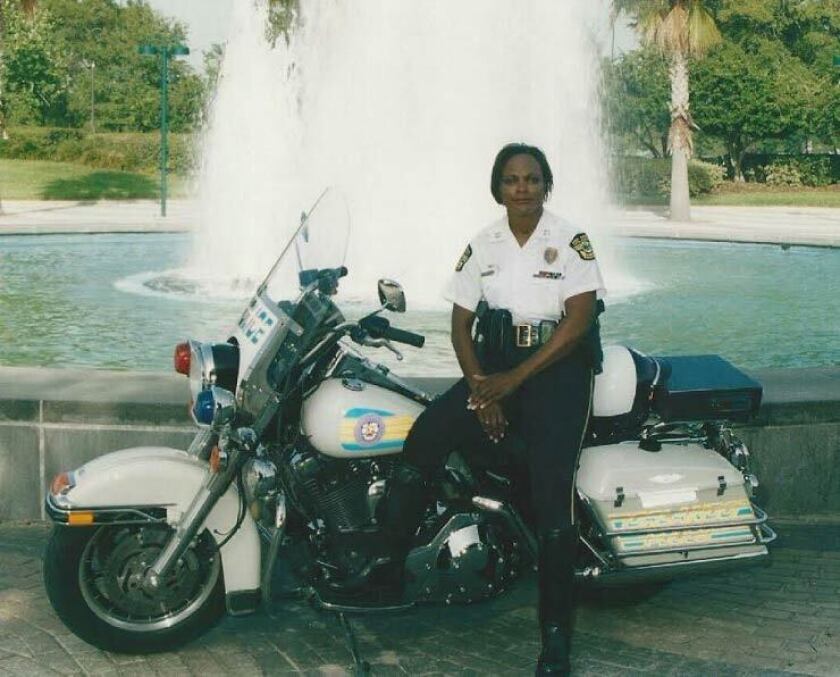 A policewoman leans against a police motorcycle in front of a fountain.
